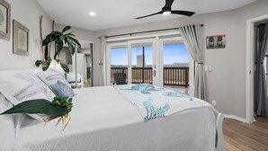 Une chambre à coucher avec un lit, un ventilateur de plafond, une grande fenêtre et une vue sur l’extérieur.