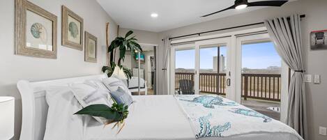 A bedroom with a bed, a ceiling fan, and a view of the outdoors.