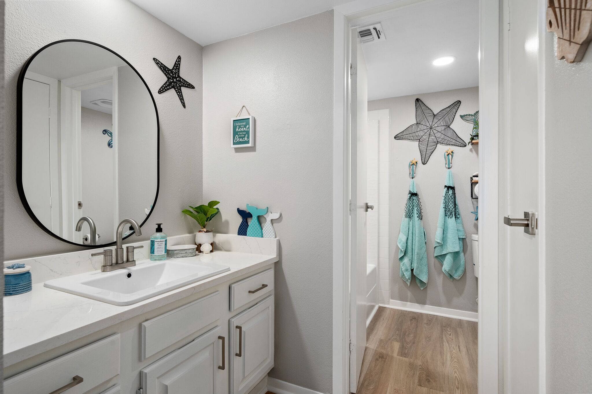 A bathroom with a white sink, two faucets, a large mirror, and a starfish decoration on the wall.