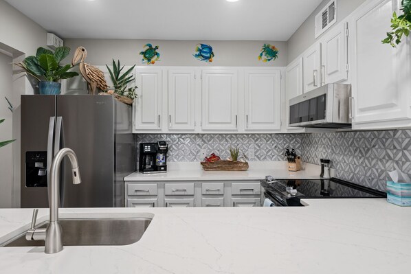 Una cocina moderna con gabinetes blancos, un refrigerador de acero inoxidable, un microondas y un fregadero.