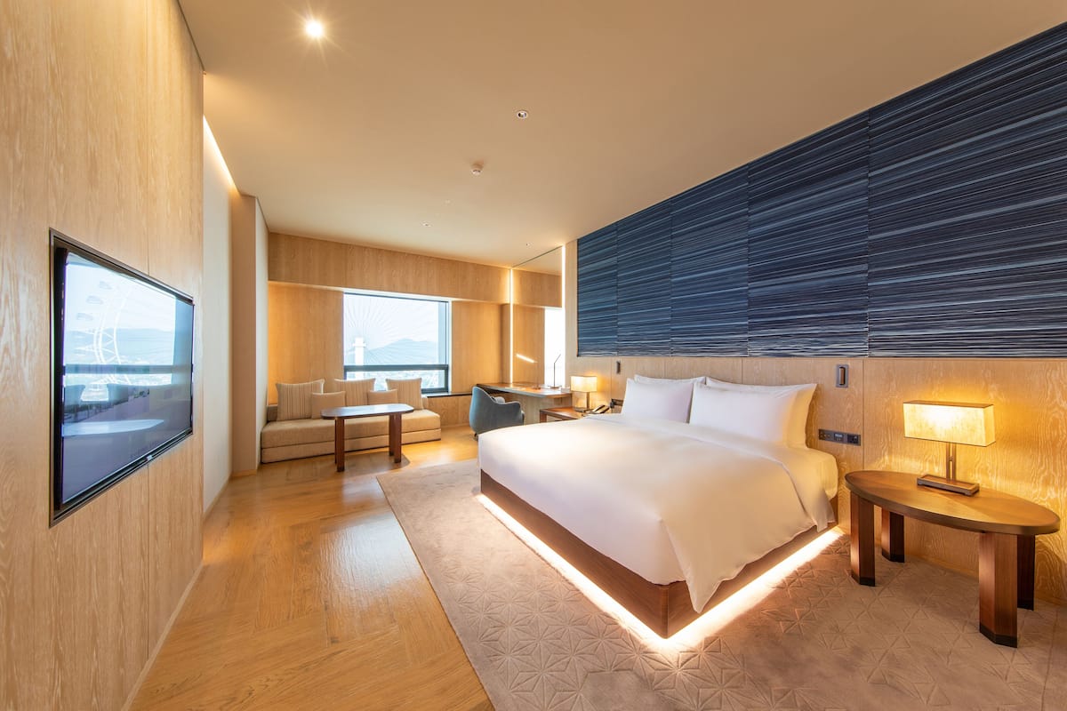A modern hotel room with a large bed, a desk, a sofa, and a TV.