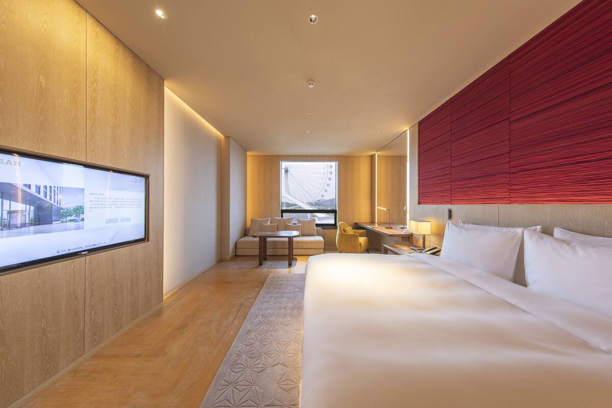 A hotel room with a large bed, a desk with a chair, a sofa, and a TV mounted on the wall.