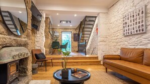 A cozy living room with a stone wall, a fireplace, a comfortable sofa, a coffee table, and a staircase leading to an upper level. - A Touch of Soho: Luxurious Historic Residence (Darlinghurst)