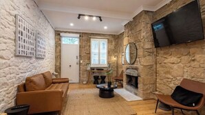 A cozy living room with a stone wall, a flat-screen TV, a fireplace, and a comfortable seating area. - A Touch of Soho: Luxurious Historic Residence (Darlinghurst)