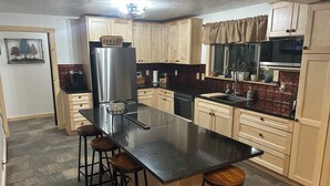 A kitchen with a central island, wooden cabinets, a stainless steel refrigerator, and a microwave. - Come ride the newly opened Argo Mine Gondola and stay ahead of the traffic. (Idaho Springs)