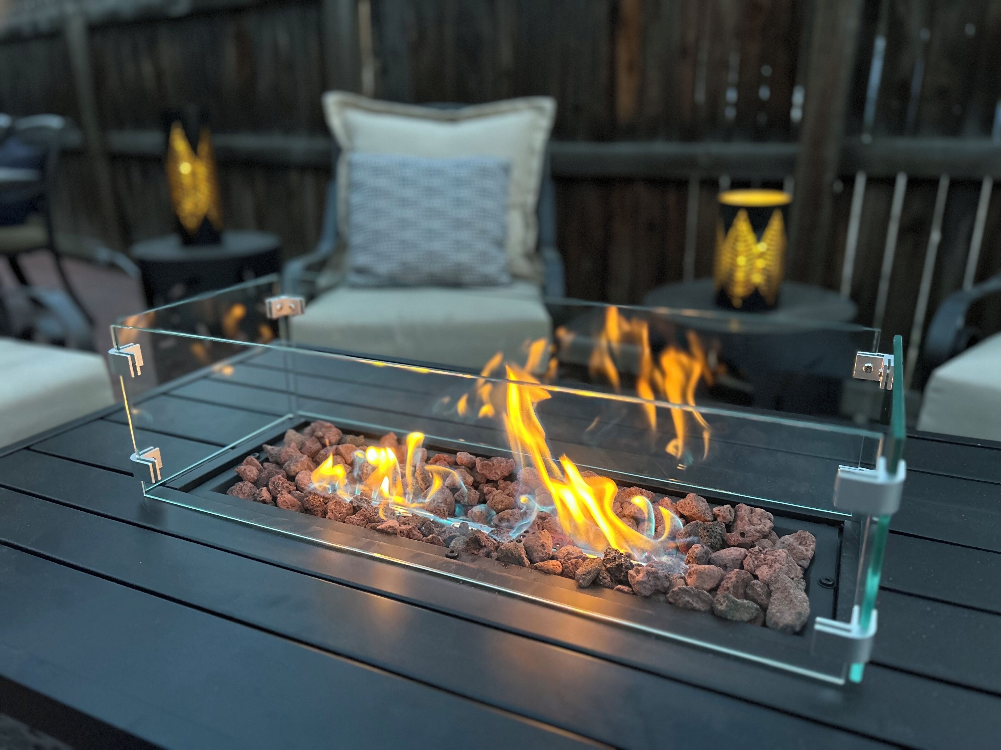 Ein Feuerkorb mit Glasabdeckung und sichtbaren Flammen, auf einem Holztisch platziert.