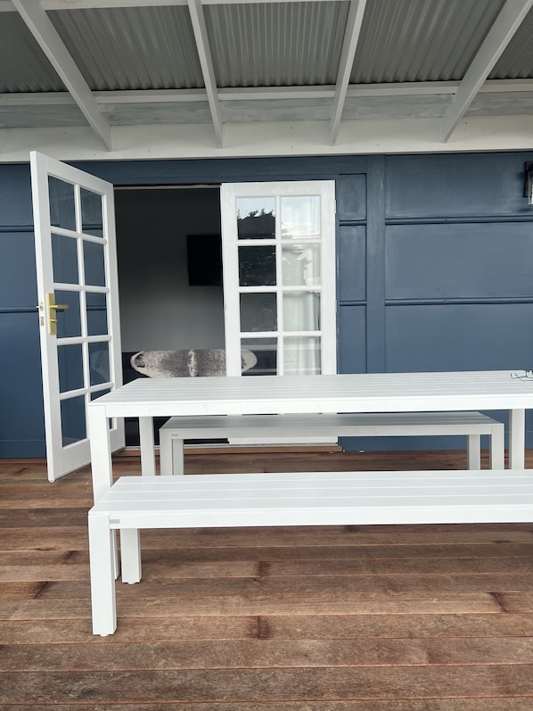 Un banco y una mesa blancos frente a una pared azul con techo metálico.