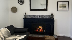 A living room with a black fireplace, a dark-colored sofa, a patterned rug, and a small wooden chest.