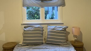 A bed with striped bedding, a window with a view of greenery, and a bedside lamp.