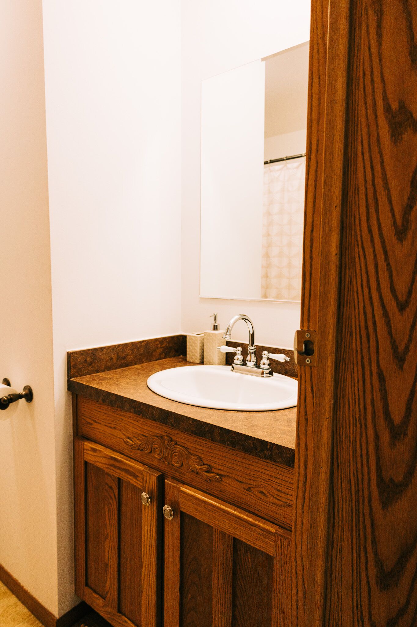 A bathroom with a wooden vanity, a white sink, and a mirror.