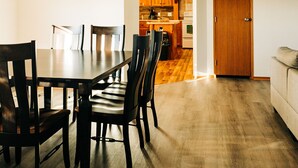 Comedor con mesa y sillas de madera, cocina al fondo y una puerta a la derecha.