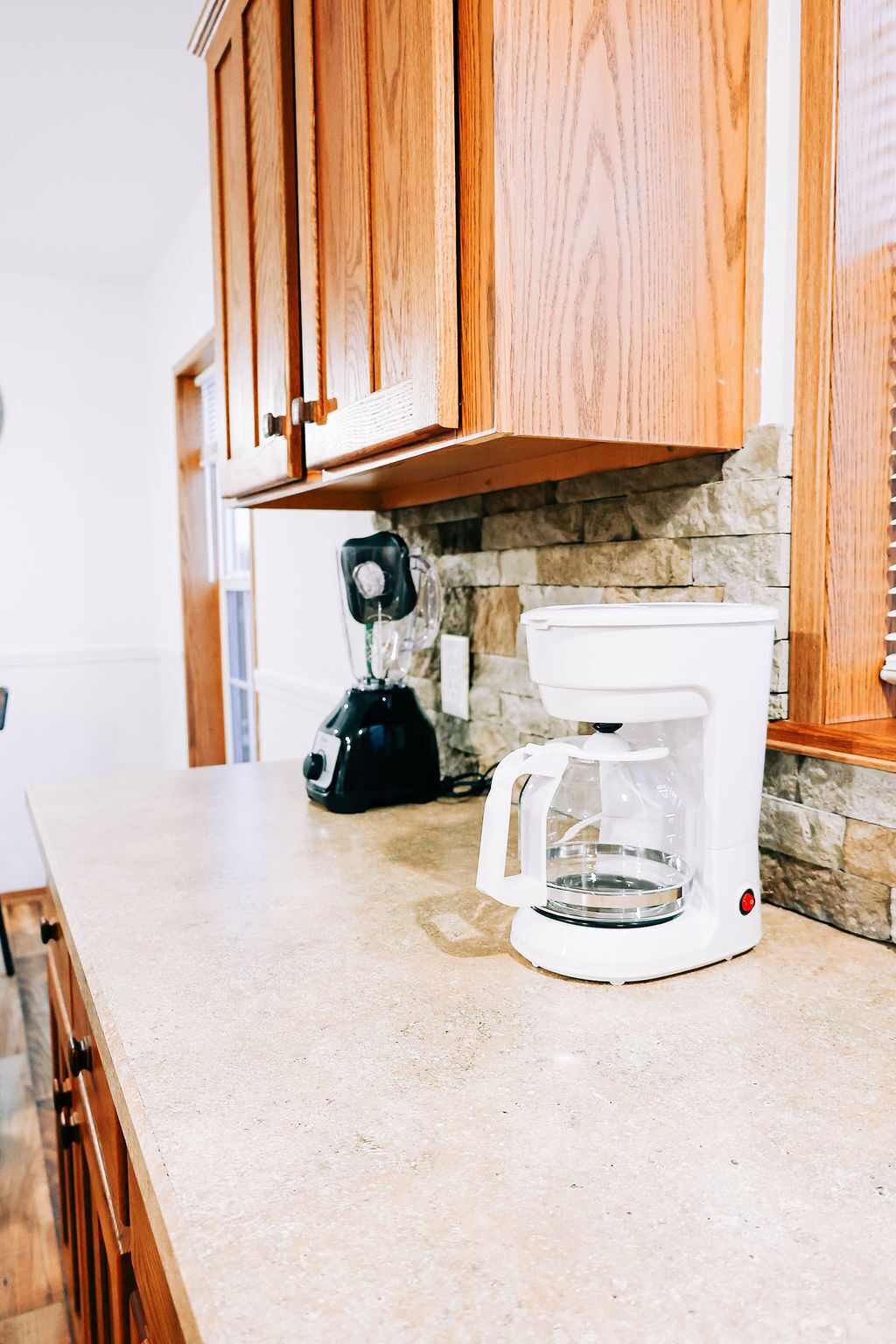 A kitchen with wooden cabinets, a stone backsplash, and a coffee maker on the counter.