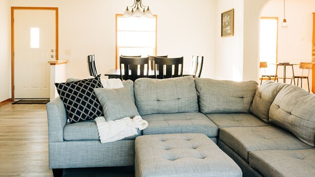 Una sala moderna con un sofá modular, un reposapiés y un comedor con sillas y una mesa.