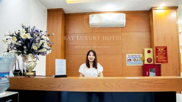A reception desk at Bay Luxury Hotel with a wooden panel design, a water dispenser, and a floral arrangement. - Hana Hotel by Bay Luxury (Hanoi)