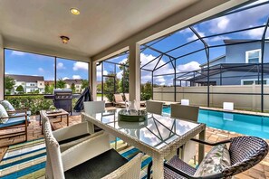 An outdoor patio with a glass table, wicker furniture, and a pool.