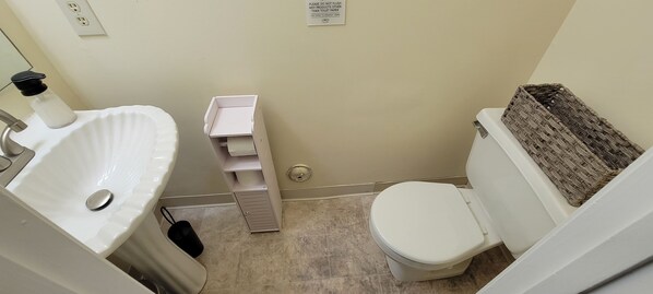 Une petite salle de bain avec un lavabo blanc, des toilettes et une poubelle.