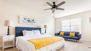Une chambre à coucher avec un lit, un canapé bleu, un ventilateur de plafond et une fenêtre avec des stores.