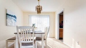 Un coin repas avec une table et des chaises blanches, un lustre et un tableau au mur.