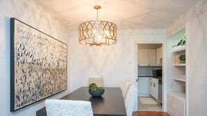 A dining area with a dark wooden table, white patterned chairs, a chandelier, and a large abstract painting on the wall.