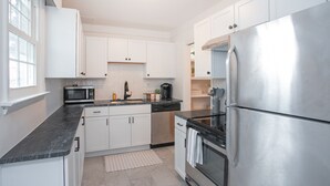 A modern kitchen with white cabinets, a stainless steel refrigerator, a microwave, and a dishwasher.