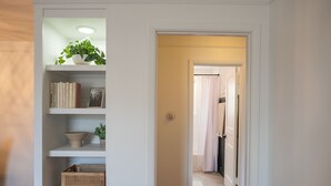 A hallway with a white shelving unit containing books, a plant, and a decorative bowl.