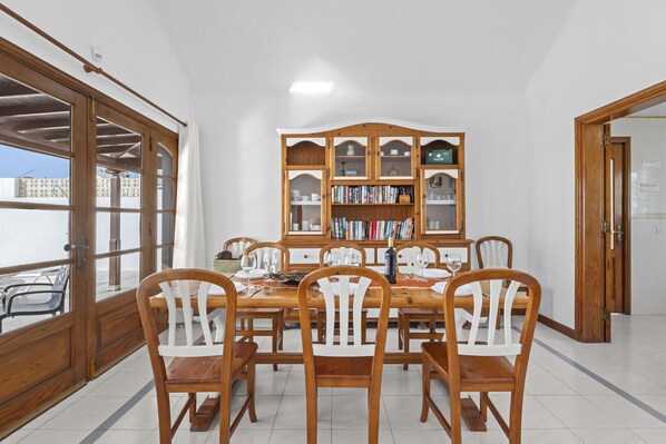 A dining area with a wooden table and chairs, a bookshelf, and a view through a glass door. - Villa Eva - Villasexperience (Puerto del Carmen)