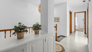 A spacious hallway with white walls, a wooden railing, and a staircase leading to another room. - Casa Estay | Holiday Apartment in Lanzarote - Spain (Playa Honda)