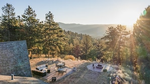 Un espace patio aménagé avec du mobilier d’extérieur, un foyer et une vue sur une vallée boisée.