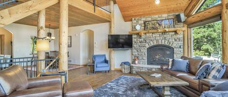 A spacious living room with a stone fireplace, leather sofas, and a high wooden ceiling.