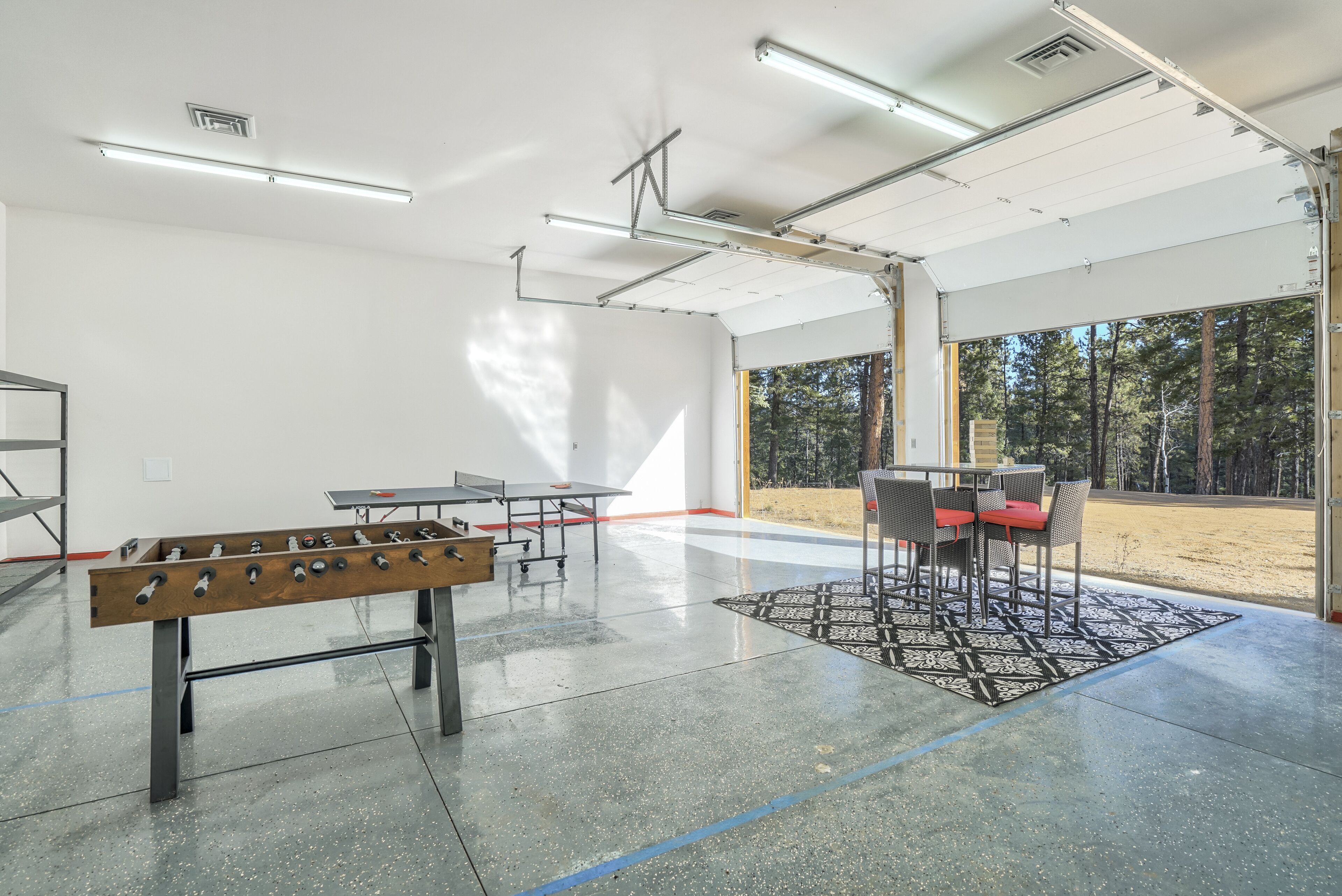 A spacious indoor area with a foosball table, ping pong table, and a seating area with chairs and a table.