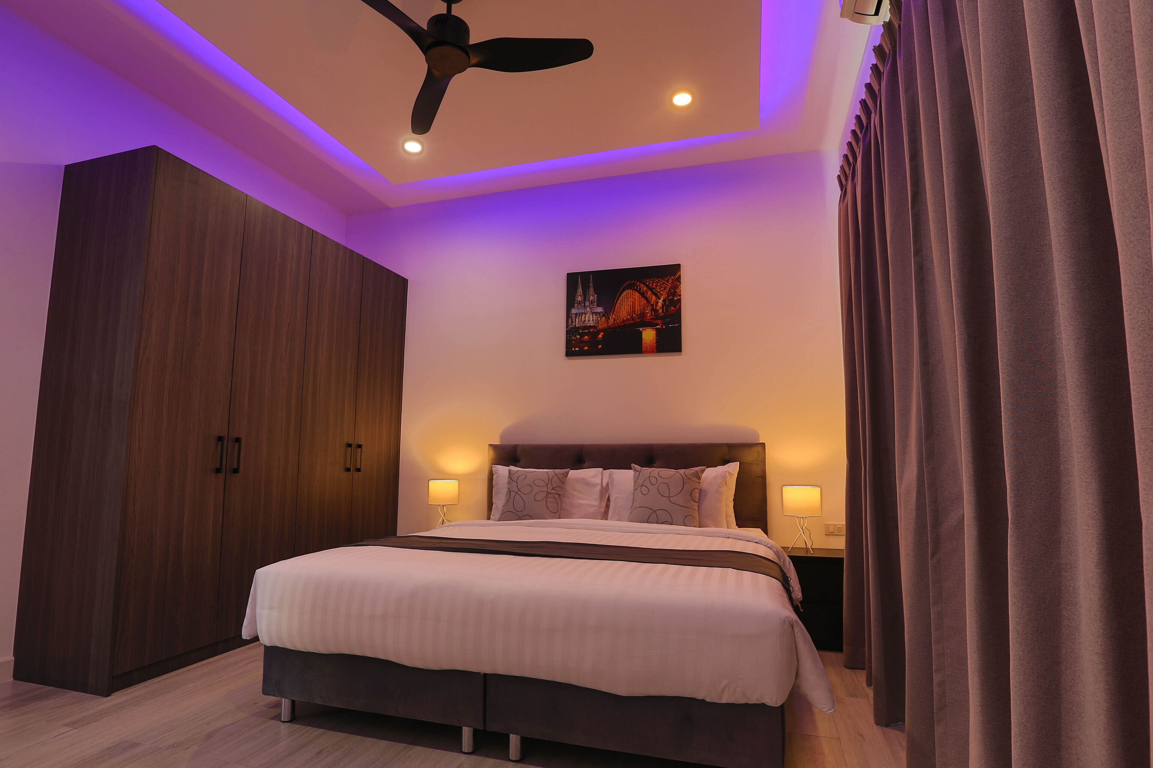 A bedroom with a bed, a ceiling fan, a nightstand, a lamp, and a wardrobe.