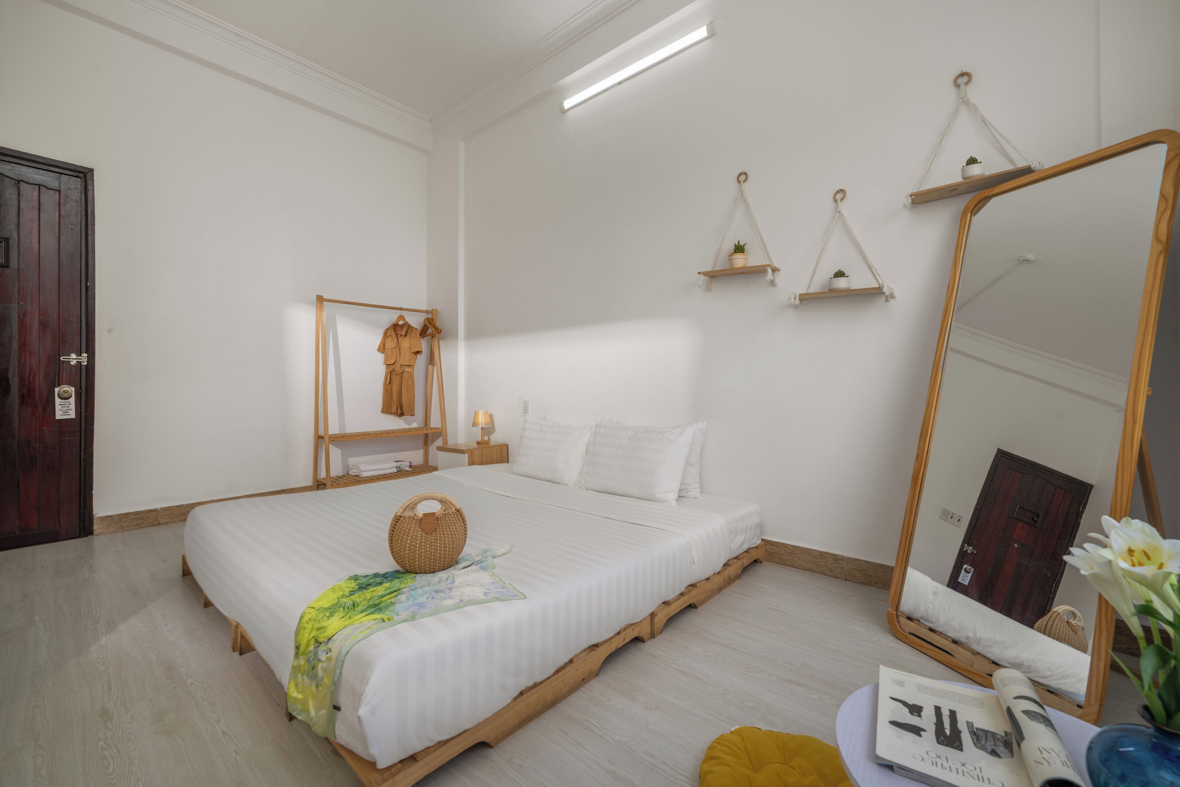 Une chambre à coucher bien rangée, avec un lit, une table de chevet, un miroir et des étagères murales.