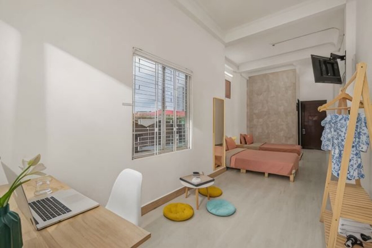 A bedroom with a bed, a desk with a laptop, a window, and a TV mounted on the wall.