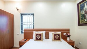 Ein Hotelzimmer mit einem Holzschrank, einem Bett mit weißer Bettwäsche und zwei Zierkissen, einem Nachttisch mit Fernbedienung, einem Fenster mit Metallgitter und einem gerahmten Gemälde an der Wand.