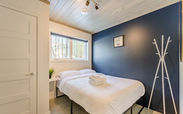 A bedroom with a bed, a window, a coat rack, and a door. - The Experience SÔ Lodge (SHEFFORD)