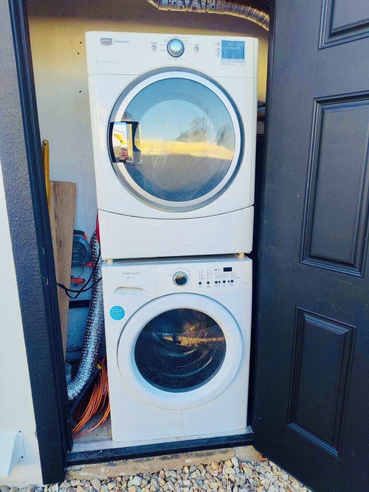 A stacked washer and dryer unit installed against a door, with visible electrical cords and a label indicating energy efficiency.