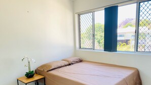 Una habitación pequeña y limpia con una cama individual, una mesita de noche y una ventana con vistas al exterior.