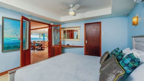 A bedroom with a bed, a ceiling fan, a painting of a beach, and a view of a dining area through an open door. - NEW Listing - Beachfront Suite & Spacious Patio (Savaneta)