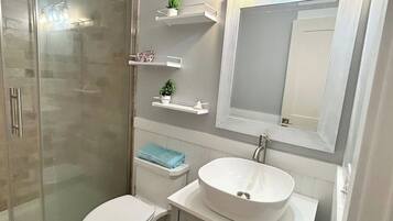 A bathroom with a glass-enclosed shower, a white sink, and a toilet.