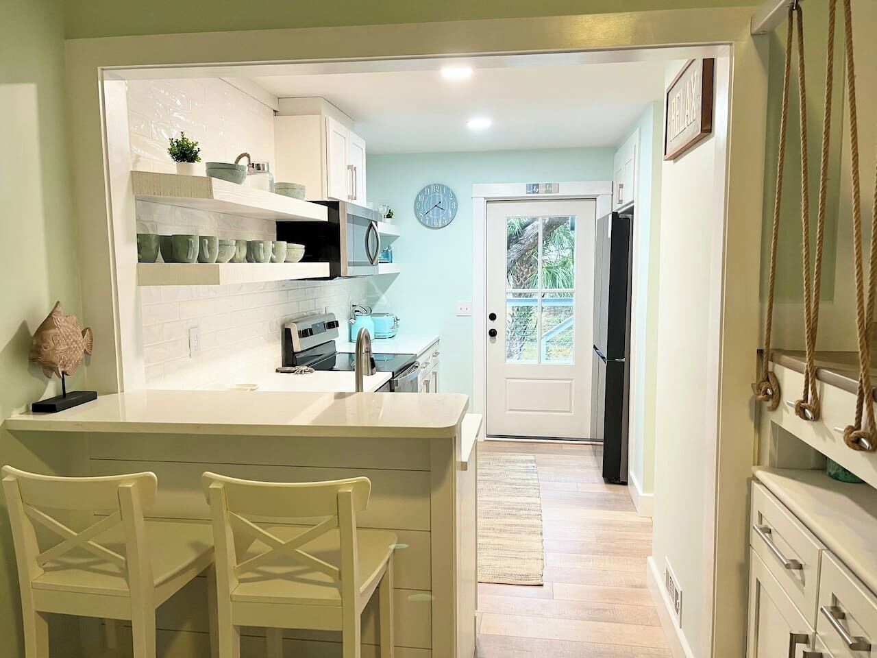 A kitchen with white cabinetry, a built-in island with chairs, a clock on the wall, and a view through the door.