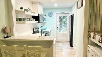A kitchen with white cabinetry, a built-in island with chairs, a clock on the wall, and a view through the door.