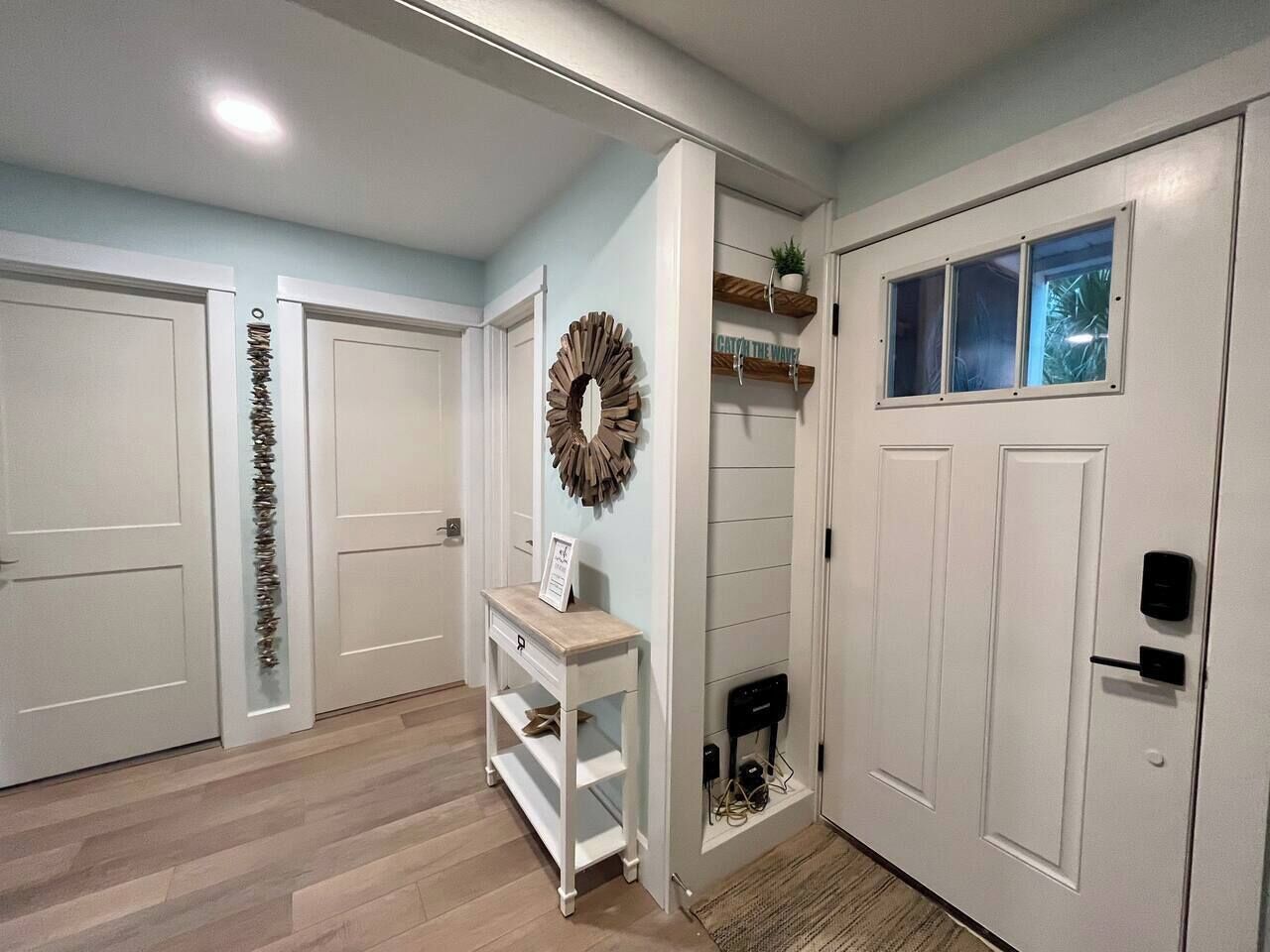 A hallway with white doors, a white console table, a decorative wreath, and a window with a view.
