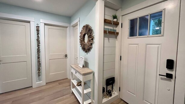 A hallway with white doors, a white console table, a decorative wreath, and a window with a view. - Perfect Vacation on Fripp (Fripp Island)
