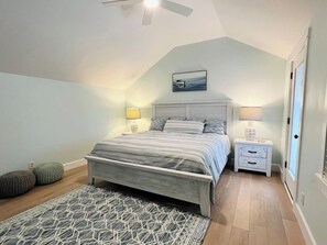Quarto com cama, mesas de cabeceira, ventoinha no teto e tapete.