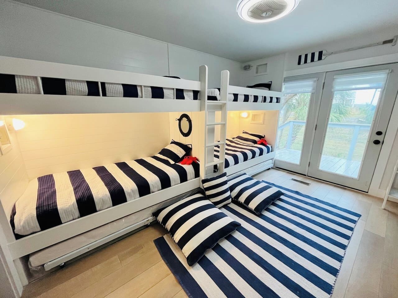 A room with bunk beds, a ladder, and a view of the outdoors through a glass door.