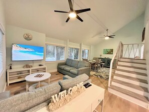 A living room with a television, sofa, coffee table, and a staircase. - Perfect Vacation on Fripp (Fripp Island)