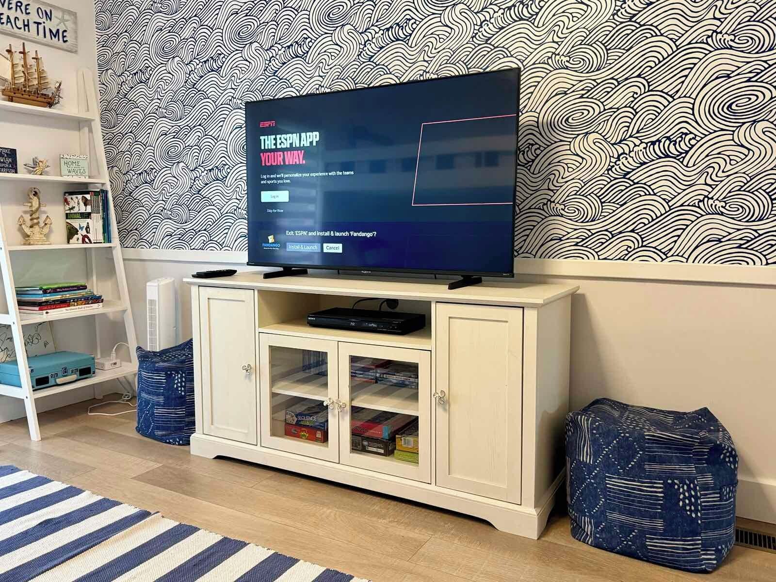 A flat-screen TV on a white cabinet with a patterned wallpaper background.