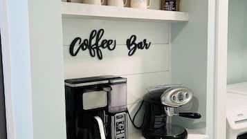 A kitchen area with a coffee bar setup, including a coffee maker, a grinder, and labeled mugs on shelves.