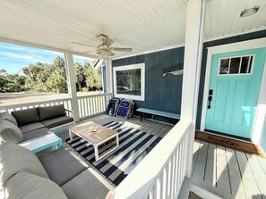 A covered porch with a sofa, a coffee table, and a ceiling fan.