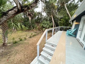 A wooden deck with a white railing, surrounded by a garden with various plants and trees.